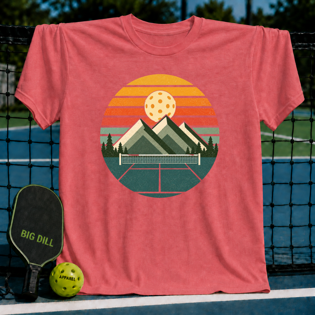 Coral unisex t-shirt featuring a retro circular graphic of mountains, a pickleball court, and a sunset over a net.