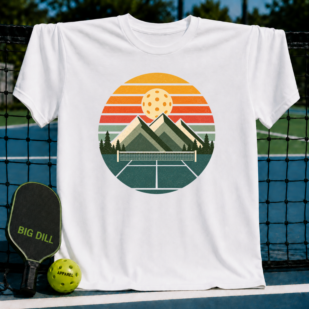 White unisex t-shirt featuring a retro circular graphic of mountains, a pickleball court, and a sunset over a net.