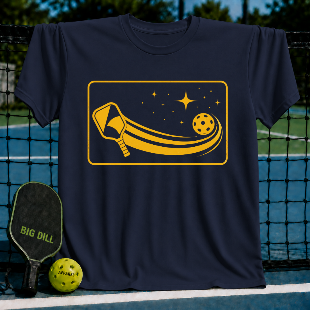 Navy blue unisex t-shirt featuring a yellow cosmic pickleball paddle and ball graphic on a pickleball court background.