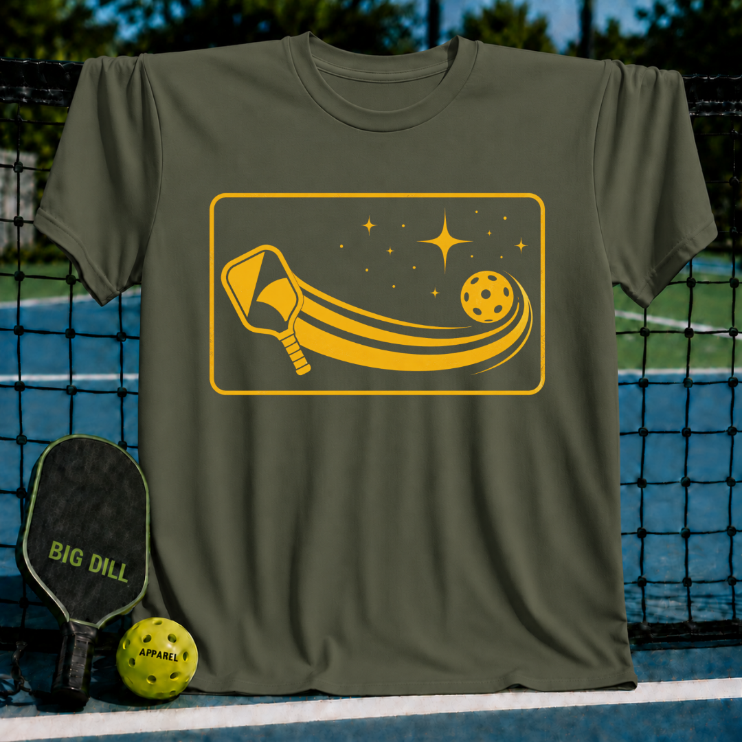 Olive green unisex t-shirt featuring a yellow graphic of a pickleball paddle and ball in a starlit cosmic arc design.