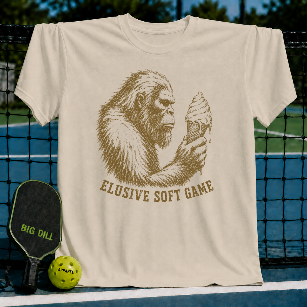 Light beige t-shirt featuring a brown Sasquatch illustration holding an ice cream cone with the text Elusive Soft Game.