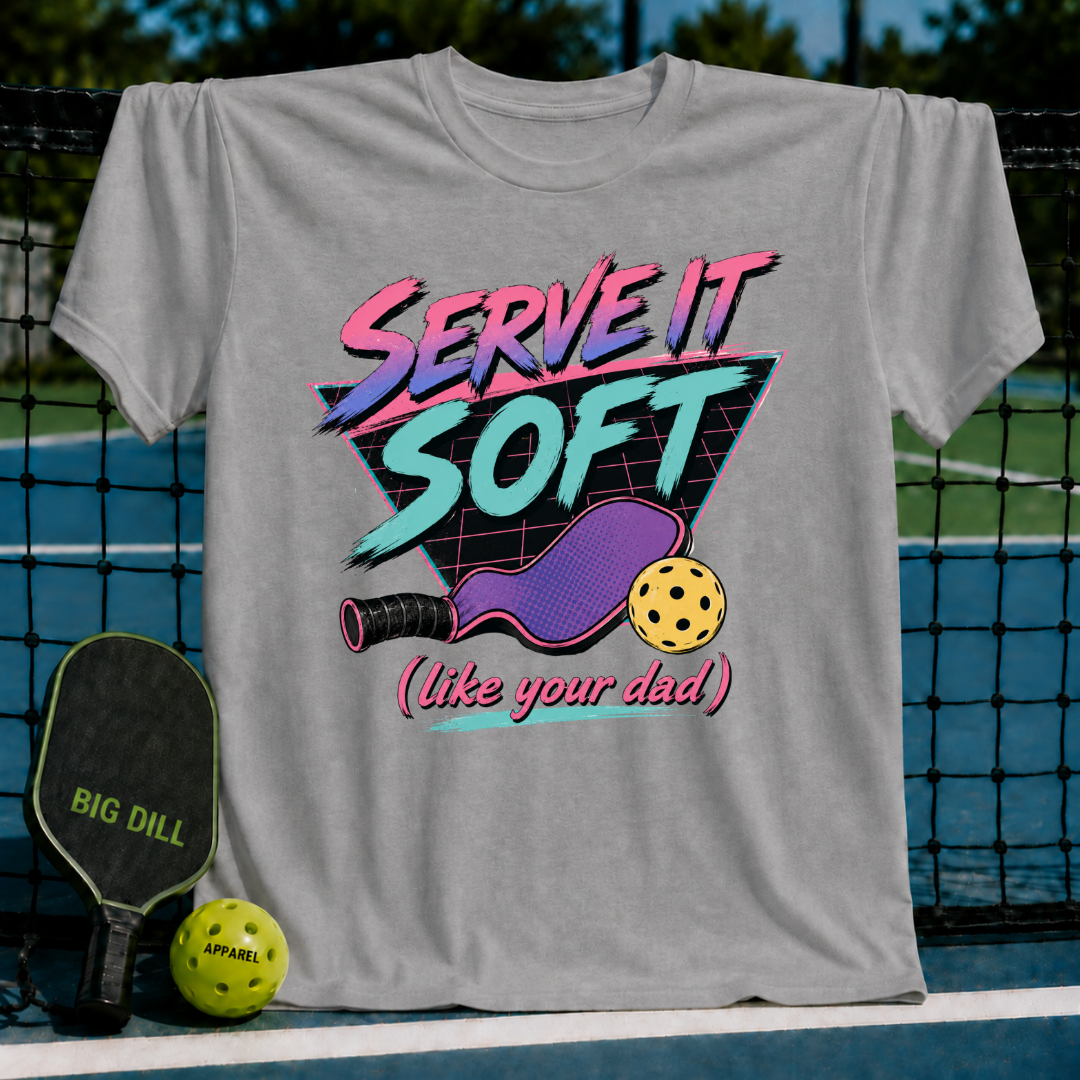 Slate blue unisex t-shirt featuring an 80s neon graphic of a pickleball paddle and ball with retro text.