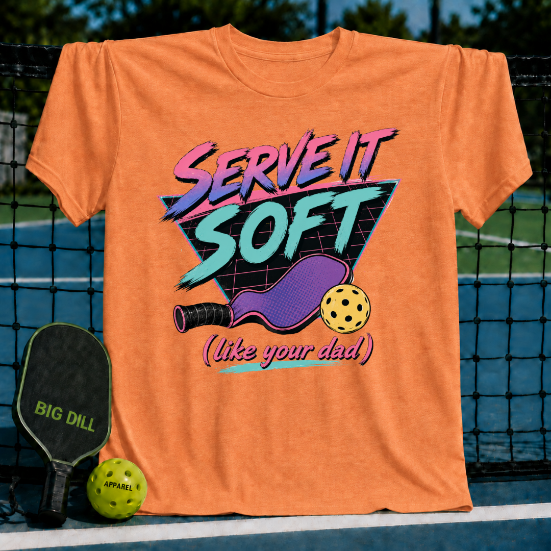 Orange unisex t-shirt featuring an 80s neon graphic of a pickleball paddle, ball, and the text Serve It Soft Like Your Dad.