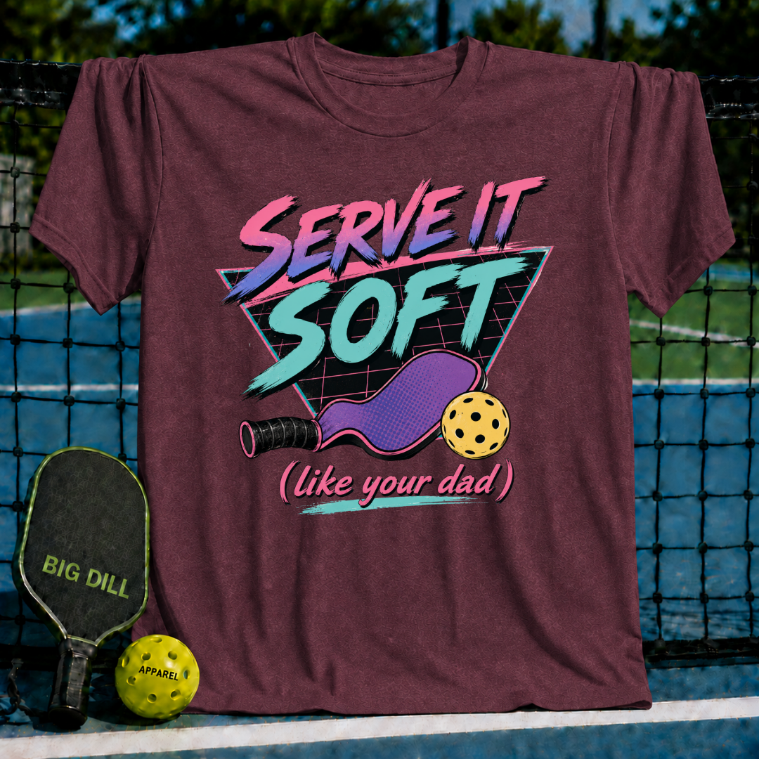 Maroon unisex t-shirt featuring an 80s neon graphic of a pickleball paddle, ball, and Serve It Soft text on a grid triangle.