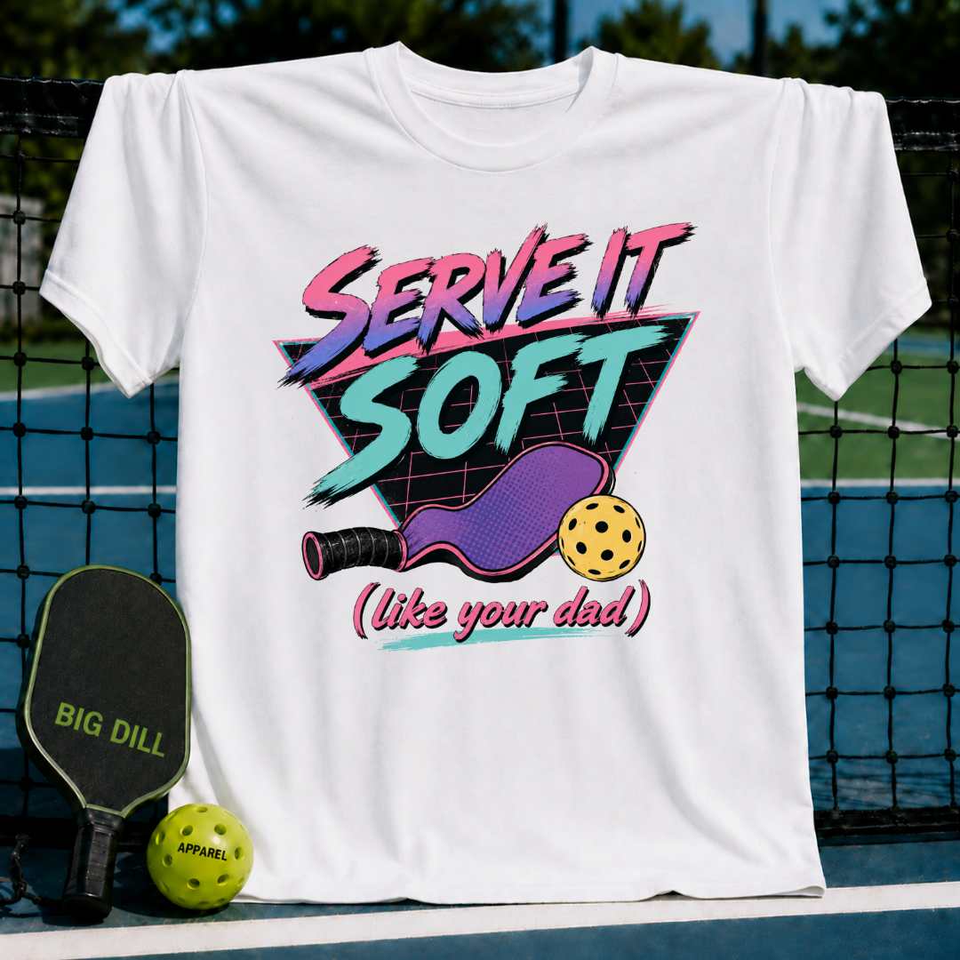 White t-shirt with 80s neon graphic of a pickleball paddle, ball, and Serve It Soft text hanging on a court net.