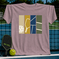 Mauve crewneck t-shirt featuring a four-panel graphic of pickleball equipment and court elements on a pickleball court.