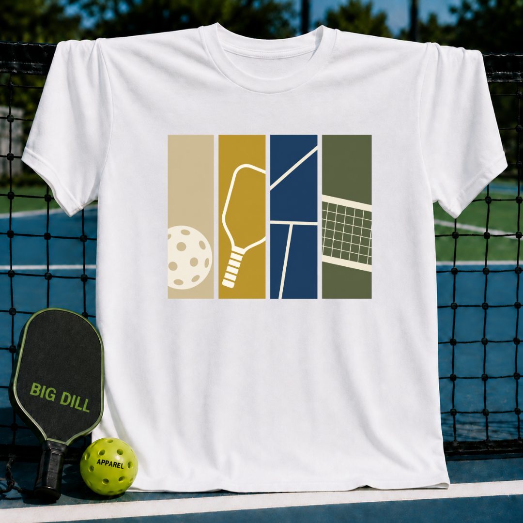 White cotton t-shirt featuring a colorful pickleball graphic with a paddle, ball, and court design on a pickleball court background.