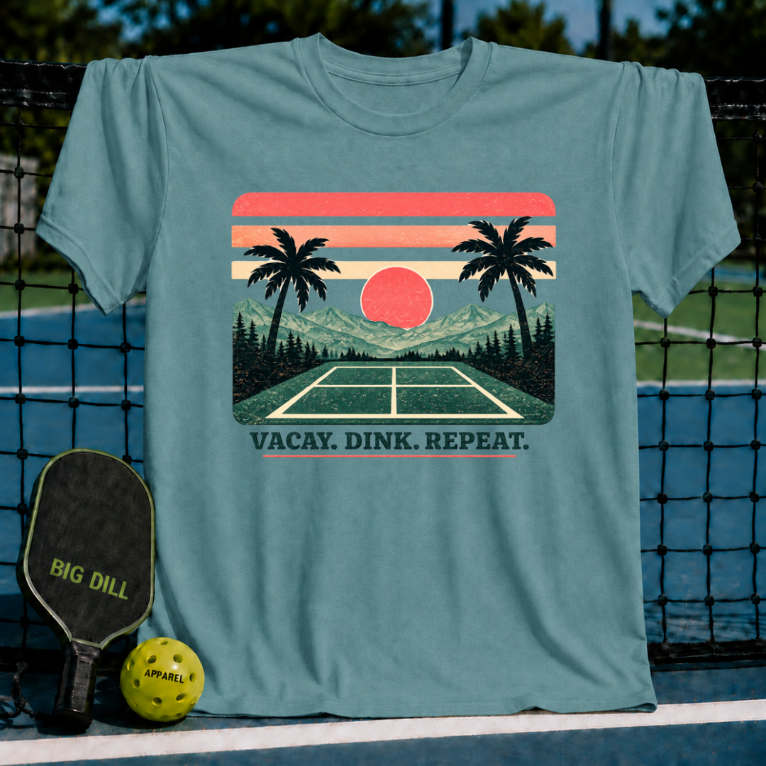Blue-grey crewneck t-shirt featuring a vintage sunset, palm tree, and pickleball court graphic with Vacay. Dink. Repeat. text.