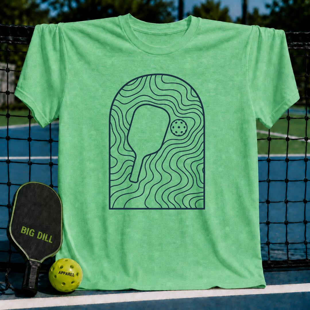 Light green unisex t-shirt featuring a minimalist slate gray arched line art graphic of a pickleball paddle and ball.