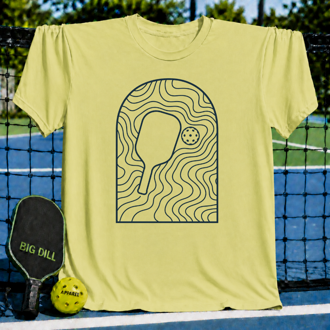 Light yellow unisex t-shirt featuring a minimalist slate gray line art graphic of a pickleball paddle and ball.