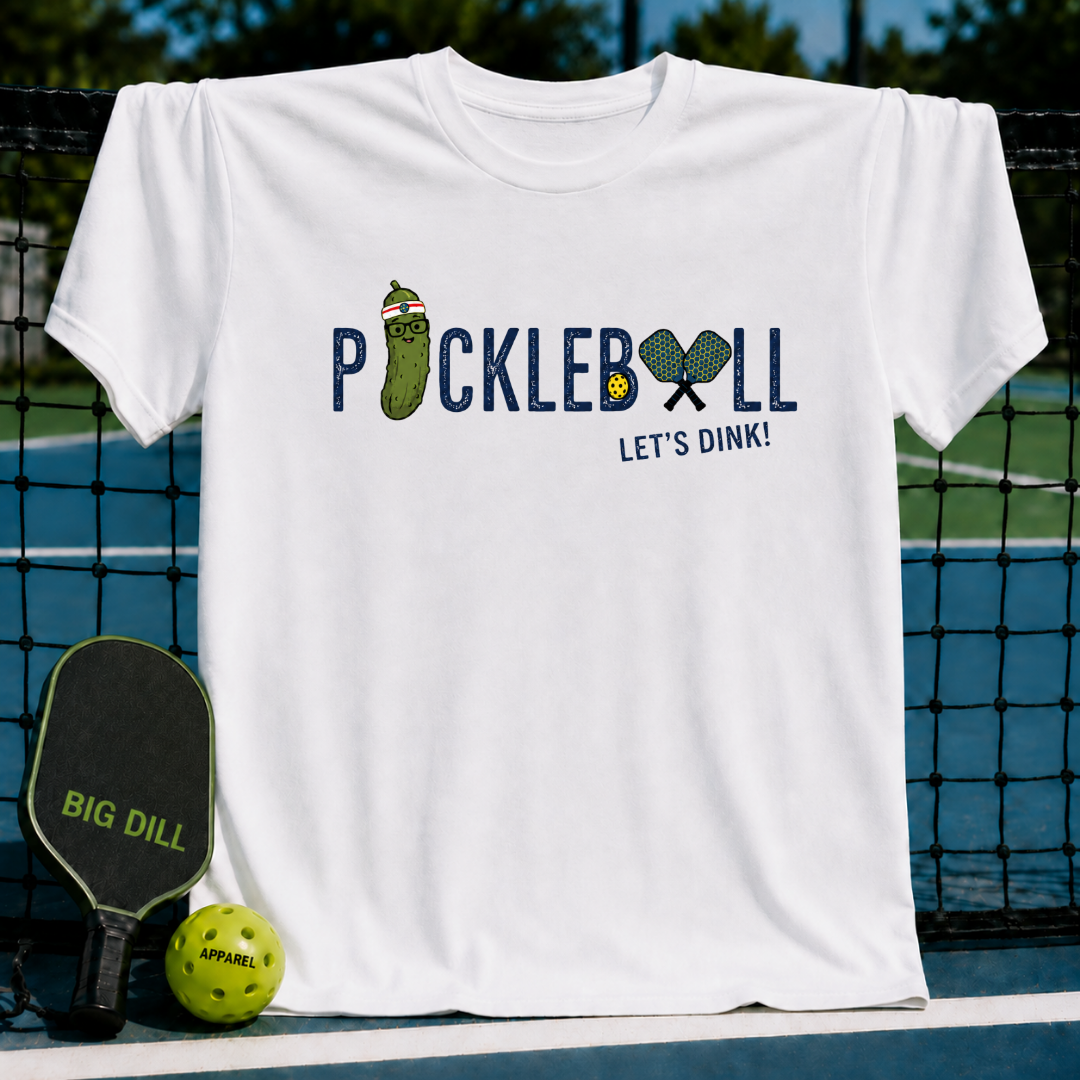 White crewneck t-shirt featuring a Pickleball Let's Dink graphic with a pickle character and paddles on a court background.