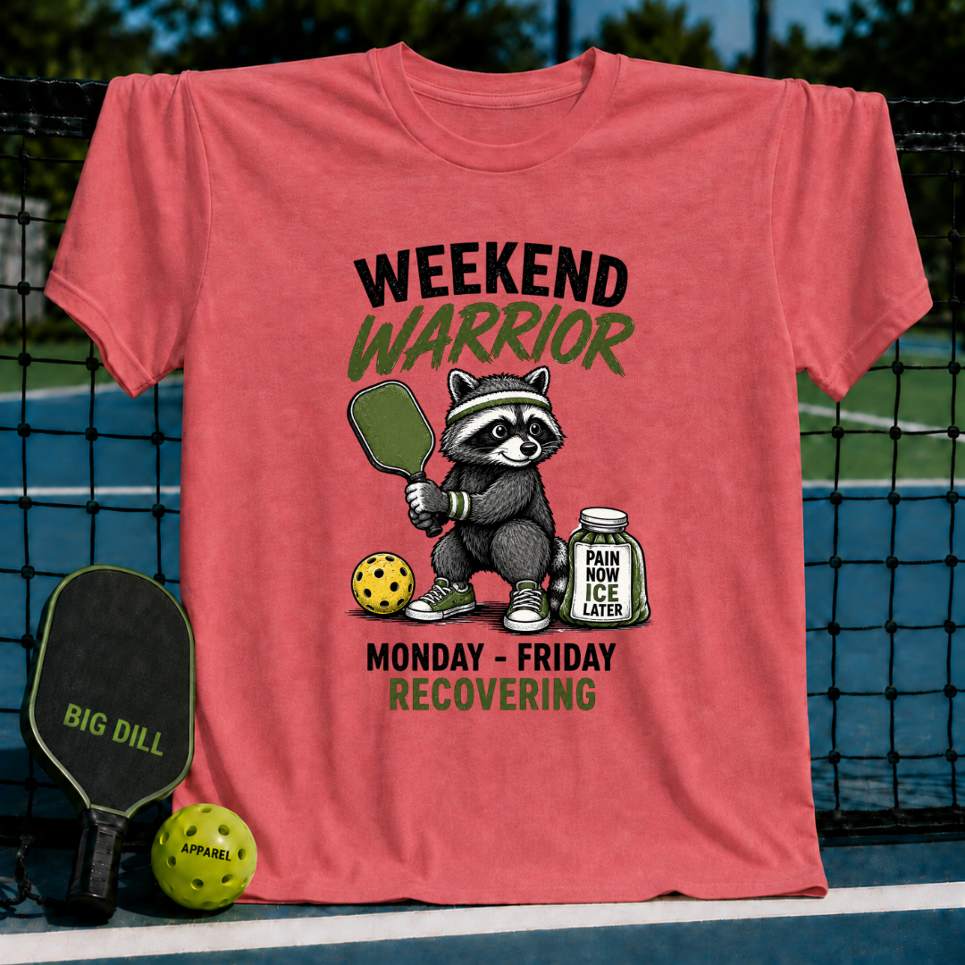 Coral-colored unisex t-shirt featuring a raccoon pickleball player graphic with the text Weekend Warrior and Pain Now, Ice Later.